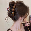 Dunkelbraunes Haar einer Frau, elegant im Dutt, verziert mit einem retro-gradienten Perlen-Haarklammer.