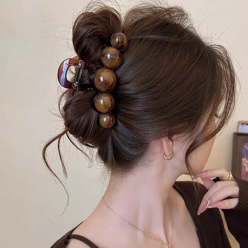 Dunkelbraunes Haar einer Frau, elegant im Dutt, verziert mit einem retro-gradienten Perlen-Haarklammer.