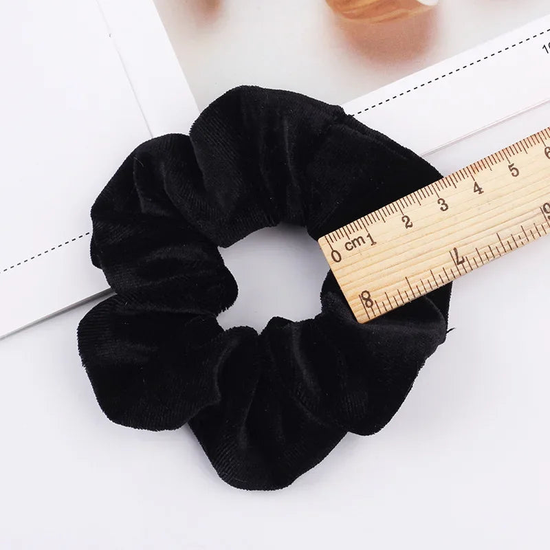 A black velvet scrunchie is shown next to a ruler for scale.