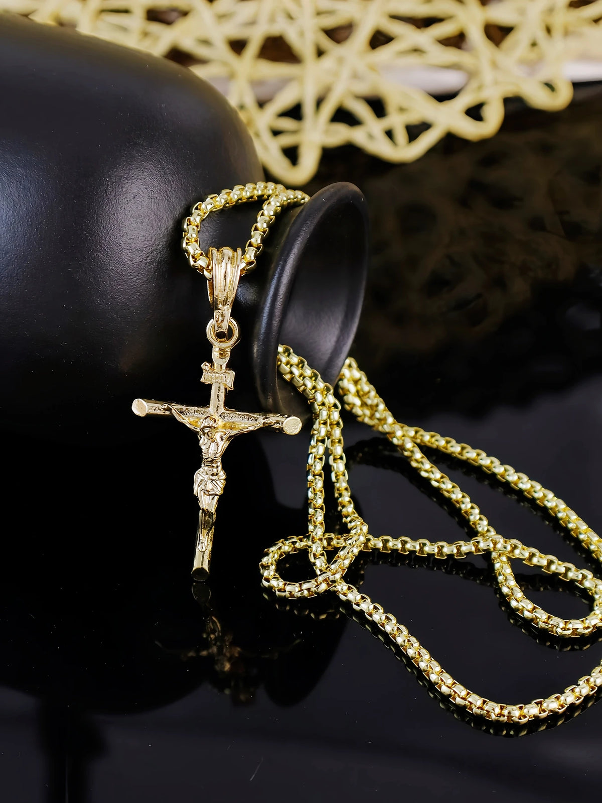 Goldplattiges Jesus-Kreuz-Anhänger-Halskette auf schwarzem Untergrund mit gelbem Spitzenhintergrund.