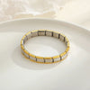 A close-up of a stainless steel charm bracelet with alternating silver and gold links resting on a white plate.