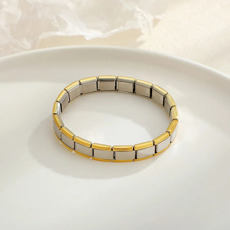A close-up of a stainless steel charm bracelet with alternating silver and gold links resting on a white plate.