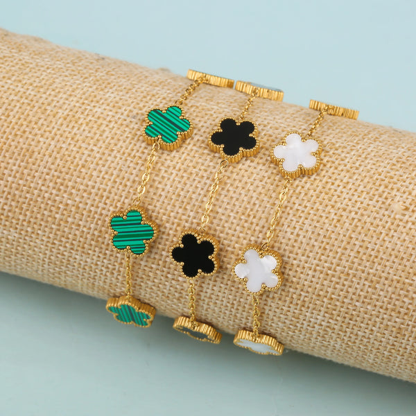 Gold plated stainless steel plant flower bracelets with green and black enamel designs on a beige fabric background