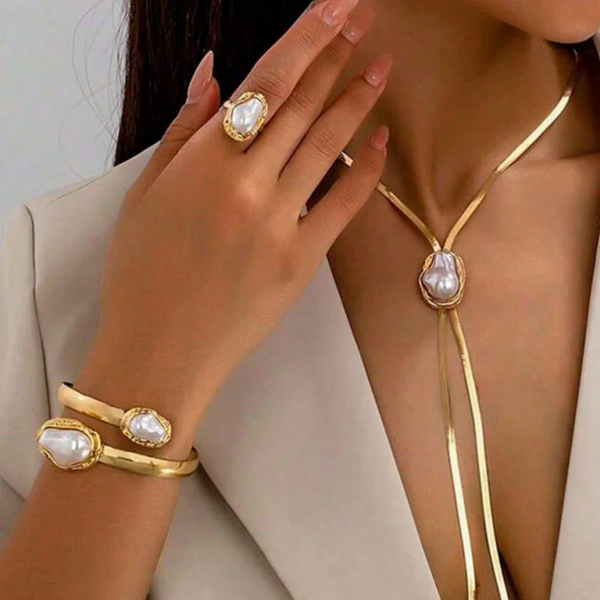 A close-up of a woman wearing a gold imitation pearl jewelry set including a ring, bracelet, and necklace.
