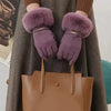 Lila Kunstfell-Handschuhe, die von einer Person gehalten werden, präsentiert vor einem braunen Mantel und einer braunen Leder