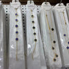 Exhibición de pulseras florales de acero inoxidable chapado en oro con cuentas azules y doradas en perchas de seda blanca.