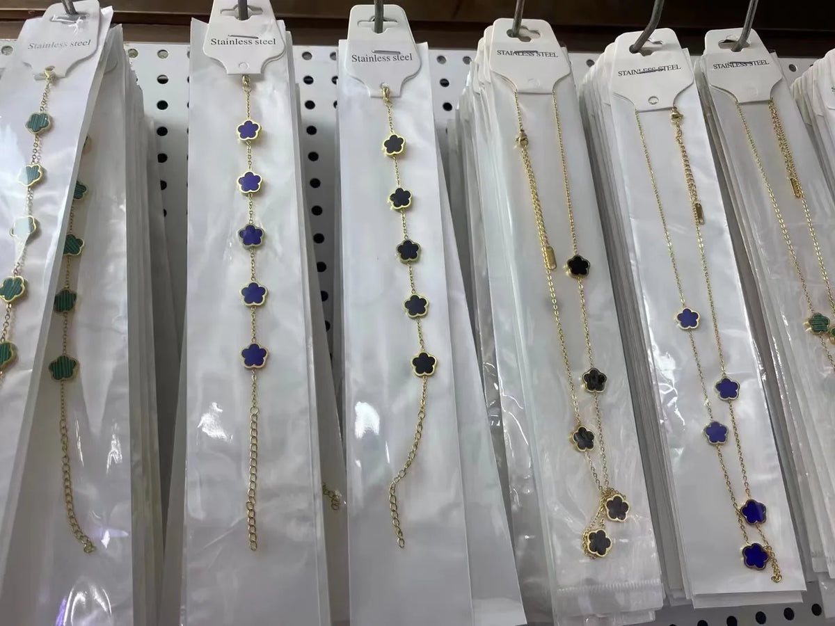 Exhibición de pulseras florales de acero inoxidable chapado en oro con cuentas azules y doradas en perchas de seda blanca.