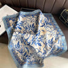 A light blue and white floral patterned silk scarf draped on a dark brown surface.