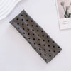 A dark gray fabric headband with small black polka dots lying on a white surface.