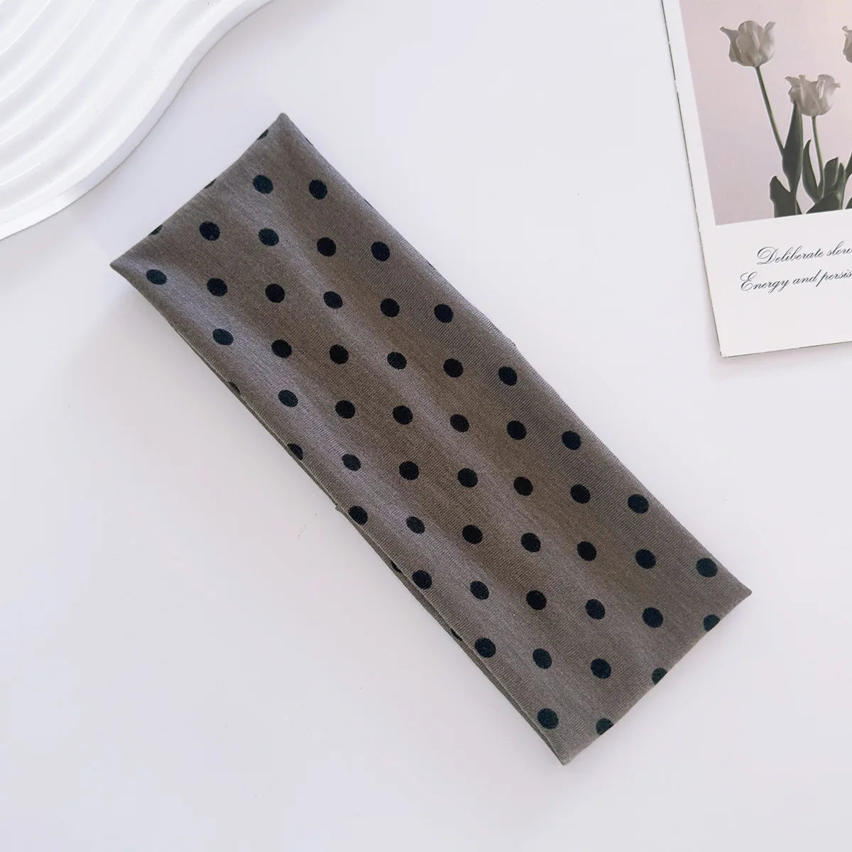 A dark gray fabric headband with small black polka dots lying on a white surface.