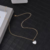 Gold chain necklace with a heart pendant displayed on a dark surface.