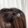 A set of adjustable hair claw clips in a dark reddish-brown color are being used to style long, dark brown hair.