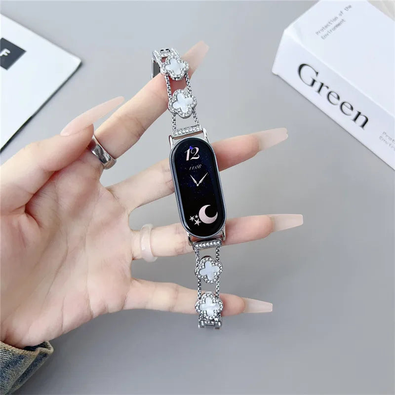 A hand holds a black smartwatch with a silver strap featuring diamond four-leaf clover accents.