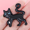 Schwarze Katzen-Email-Anstecknadel mit leuchtend blauen Augen und gekrümmtem Schwanz, gehalten von einer Hand.