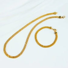 A gold plated necklace set featuring a long chain and a circular bracelet displayed against a white background.