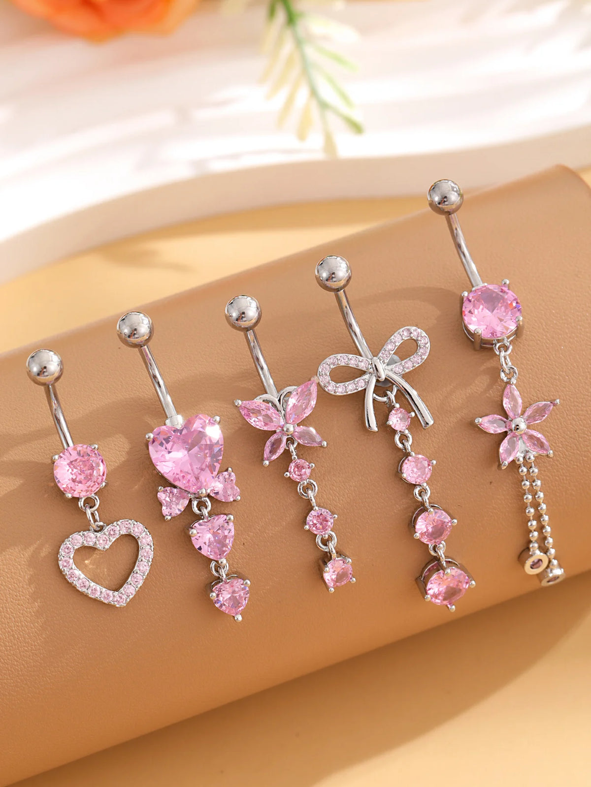 A set of five gold stainless steel dangled belly button rings featuring pink and clear stones.