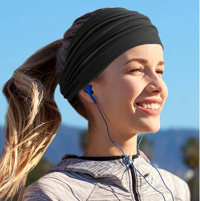 A woman wearing a black headband with a blue earphone wire, smiling outdoors.