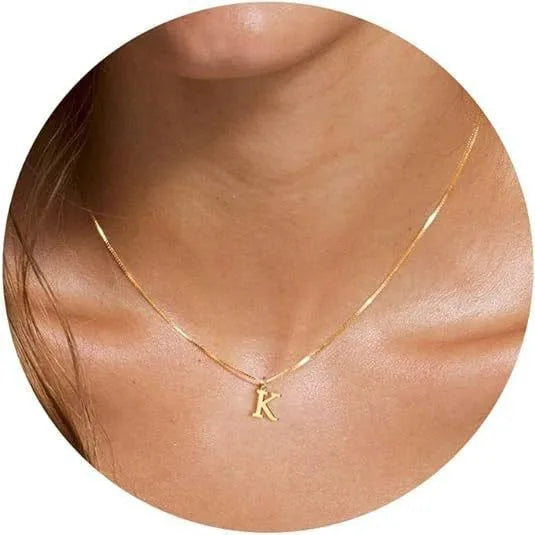 A close-up of a gold plated alphabet initial necklace with the letter K worn around the neck.