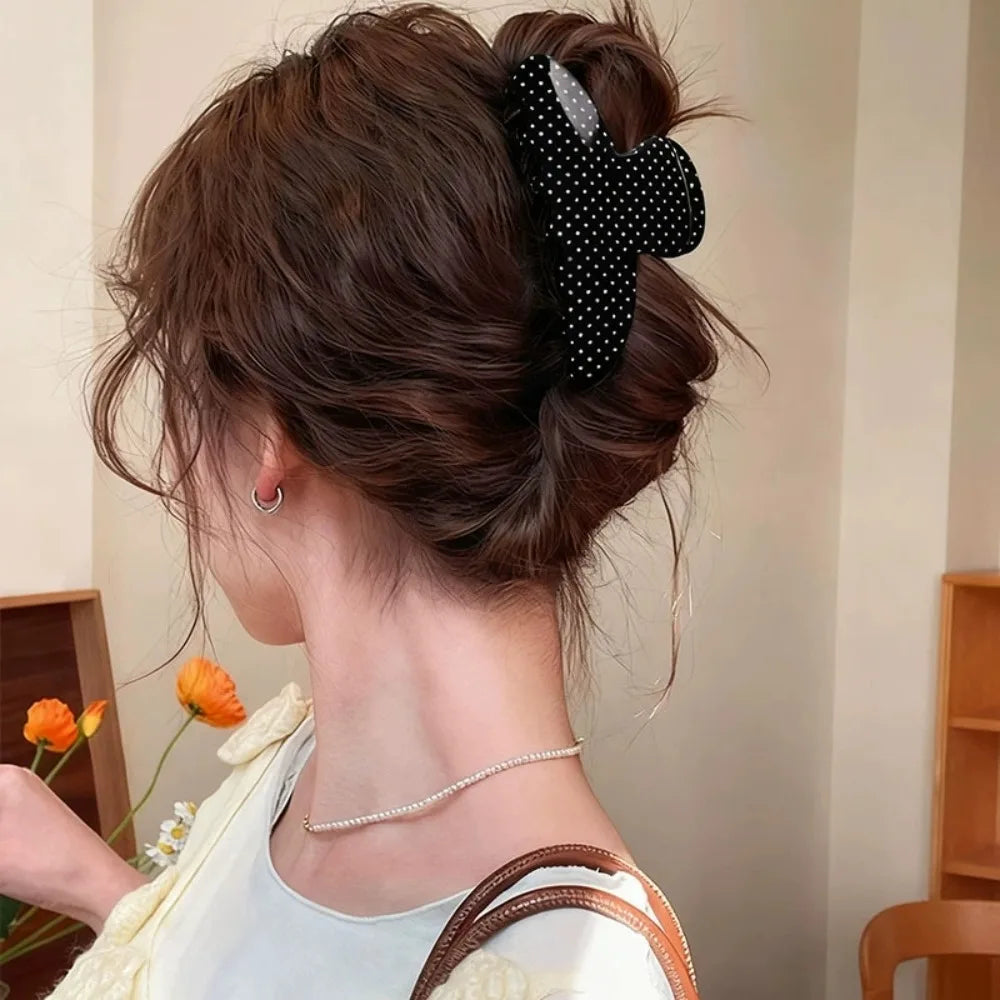 Cabello castaño oscuro recogido con horquillas de lunares negros y una blusa blanca.
