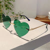 Vintage, randlose Sonnenbrille in Herzform mit grün getönten Gläsern auf weißem Untergrund.