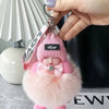 A pink fluffy plush doll with a headband and a black tag is being held by a hand.