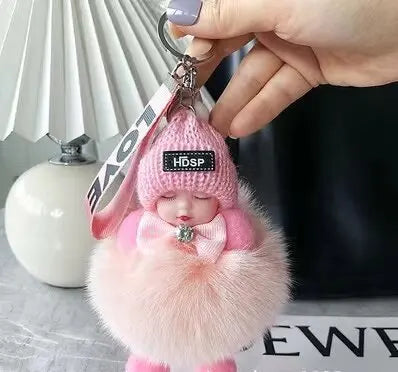 A pink fluffy plush doll with a headband and a black tag is being held by a hand.