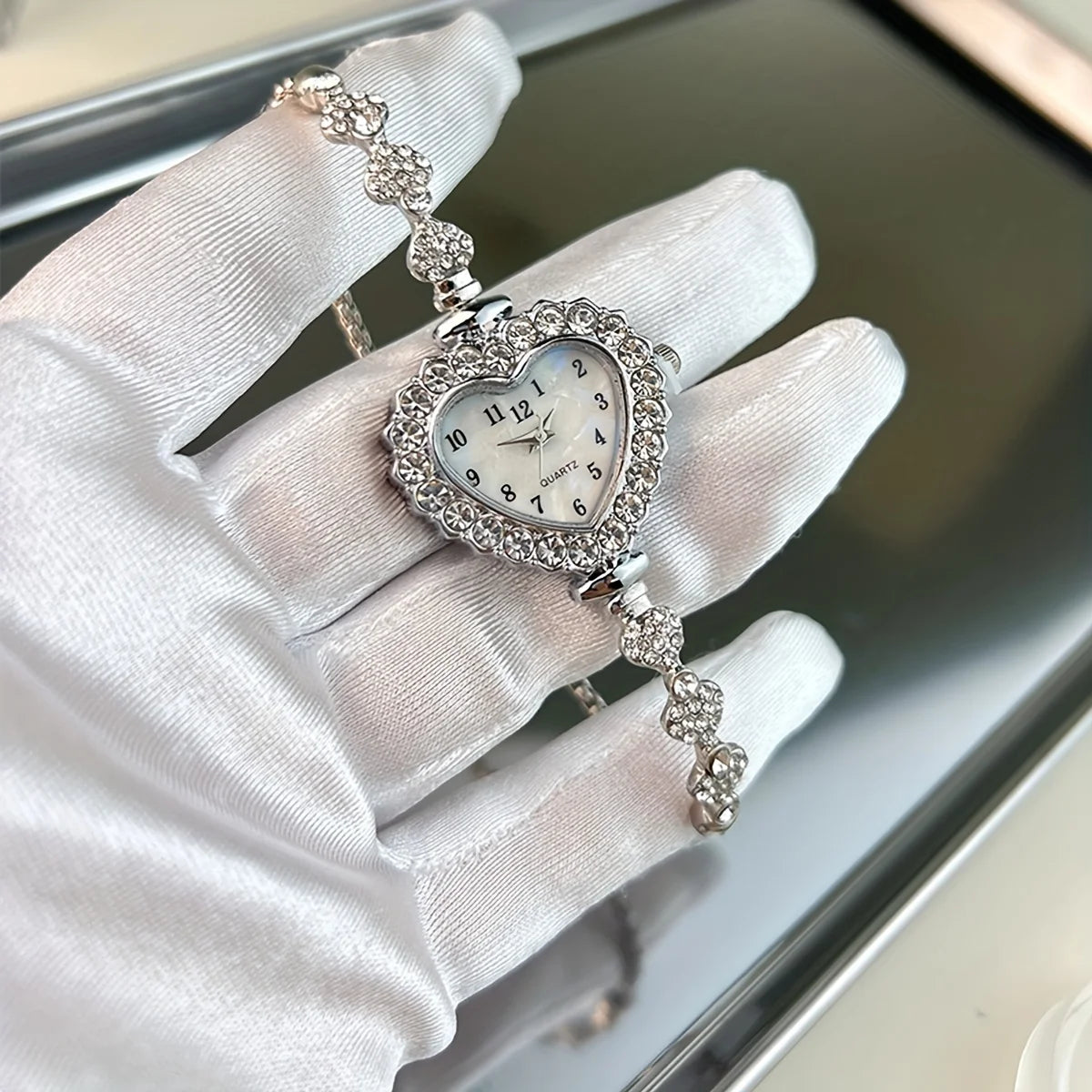 A hand wearing a white glove holds a sparkling heart rhinestone quartz watch with a silver chain.
