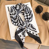 A black and white checkered silk scarf tied in a bow displayed on a beige blazer.