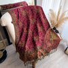 A deep maroon bohemian paisley tassel shawl draped over a light-colored chair.