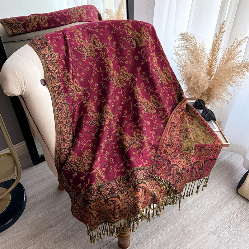 A deep maroon bohemian paisley tassel shawl draped over a light-colored chair.