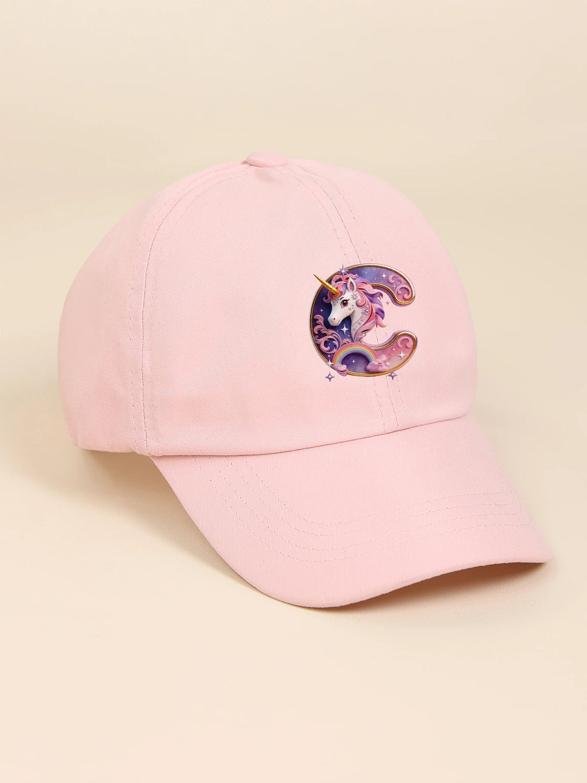 A pink baseball cap featuring a purple and iridescent unicorn letter C embroidered on the front.