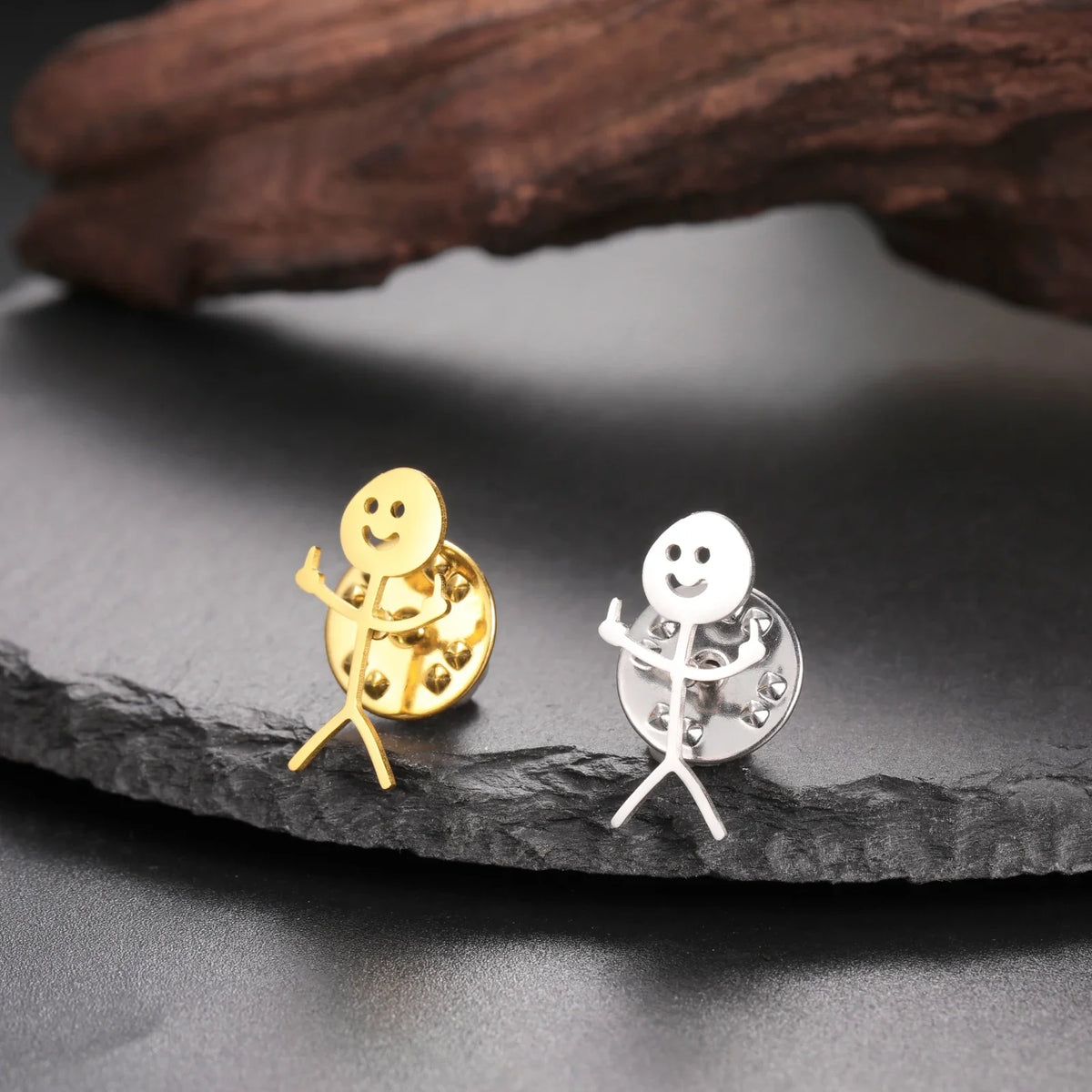 Gold and silver stickman brooches resting on a dark slate rock.