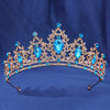 A sparkling gold crystal rhinestone tiara and headband set with blue gemstones against a dark blue background.