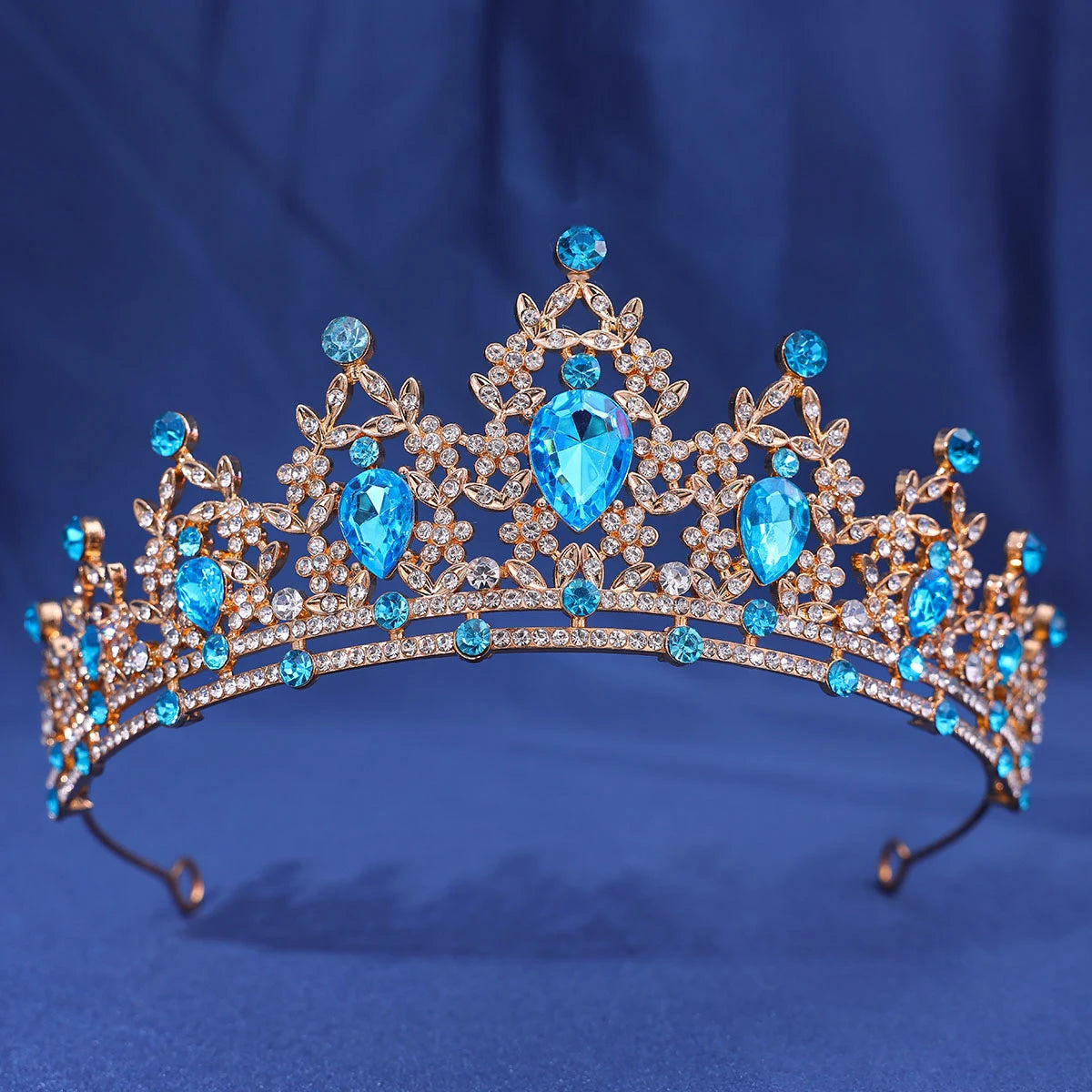 A sparkling gold crystal rhinestone tiara and headband set with blue gemstones against a dark blue background.
