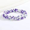 Una pulsera hecha de pequeñas cuentas moradas y blancas, enhebradas en múltiples hilos.