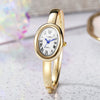 A gold-toned quartz watch bracelet with a white face and Roman numerals is displayed on a light surface.