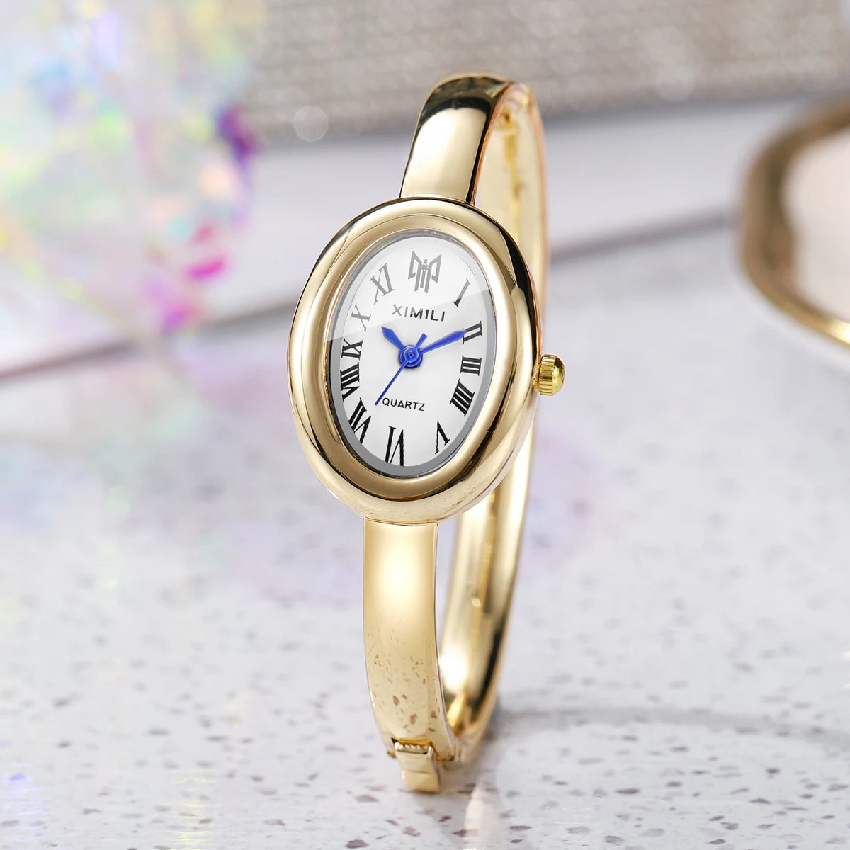 A gold-toned quartz watch bracelet with a white face and Roman numerals is displayed on a light surface.