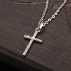 A silver stainless steel cross pendant necklace with a sparkling zircon detail resting on a dark surface.