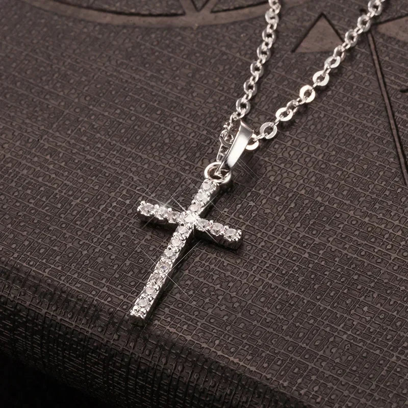 A silver stainless steel cross pendant necklace with a sparkling zircon detail resting on a dark surface.