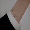 A close-up of a sterling silver double heart charm bracelet worn on a wrist against a light background.