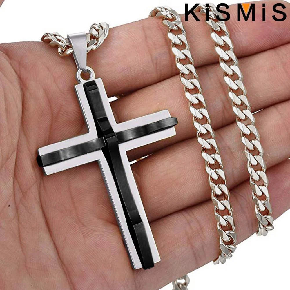 Colgante de cruz de acero inoxidable con detalles en negro y plata, mostrado en la mano de una persona.