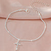 A delicate sparkling zircon heart cross anklet is displayed against a soft pink fabric background.