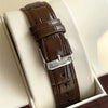 Montre à bracelet en cuir marron avec boucle argentée et logo de marque, présentée dans une boîte.