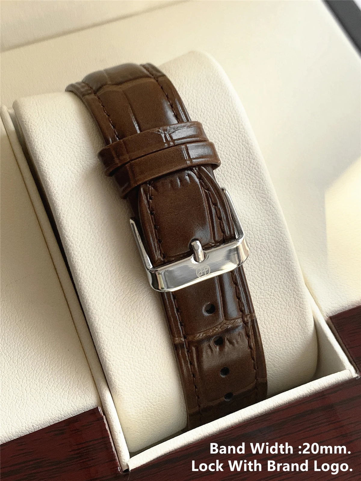 Montre à bracelet en cuir marron avec boucle argentée et logo de marque, présentée dans une boîte.