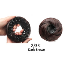 Una mano sostiene un moño de cabello sintético negro con clips elásticos, mostrando la textura y el color de cabello castaño 