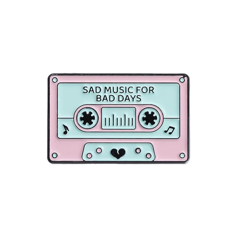 A pink and teal cassette tape enamel pin featuring the text Sad Music for Bad Days