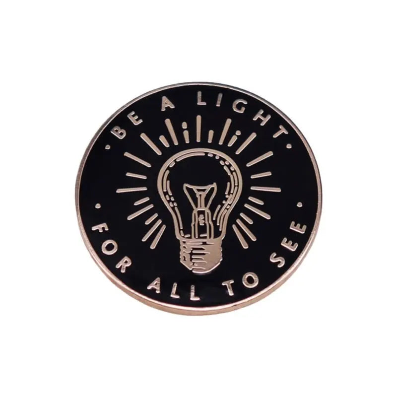 A round, copper-toned lapel pin featuring an inspirational quote design with a lightbulb silhouette.