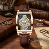 Reloj mecánico esqueleto chapado en oro rosa con correa de cuero marrón sobre una superficie de madera.