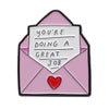 A pink envelope shaped enamel pin featuring the text You're doing a great job and a red heart detail.
