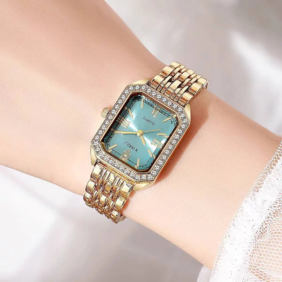 A gold-toned rhinestone quartz wristwatch with a light blue face and gold links on a woman's wrist.